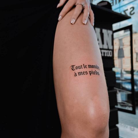 A short French phrase sits on the lower thigh just above the knee, using elegant black lettering and a restrained layout for a clean minimalist result