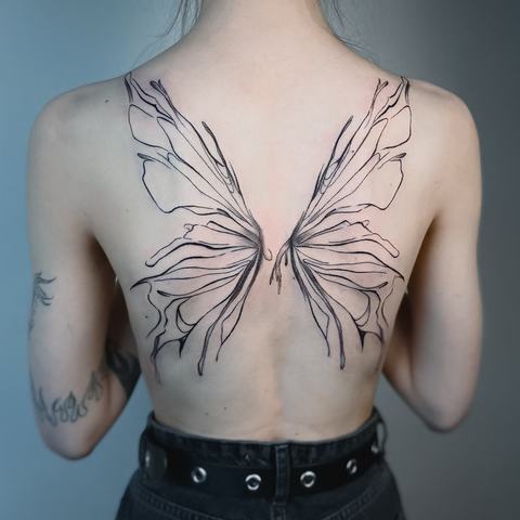 A large butterfly spreads across the upper back, with elongated fine-line wings extending over the shoulder blades in a light, symmetrical composition