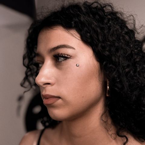Cheek dermal piercing with a refined accent placed just below the eye area. The jewellery creates a bright, minimal detail while keeping the overall look elegant, with precise placement and sterile conditions.